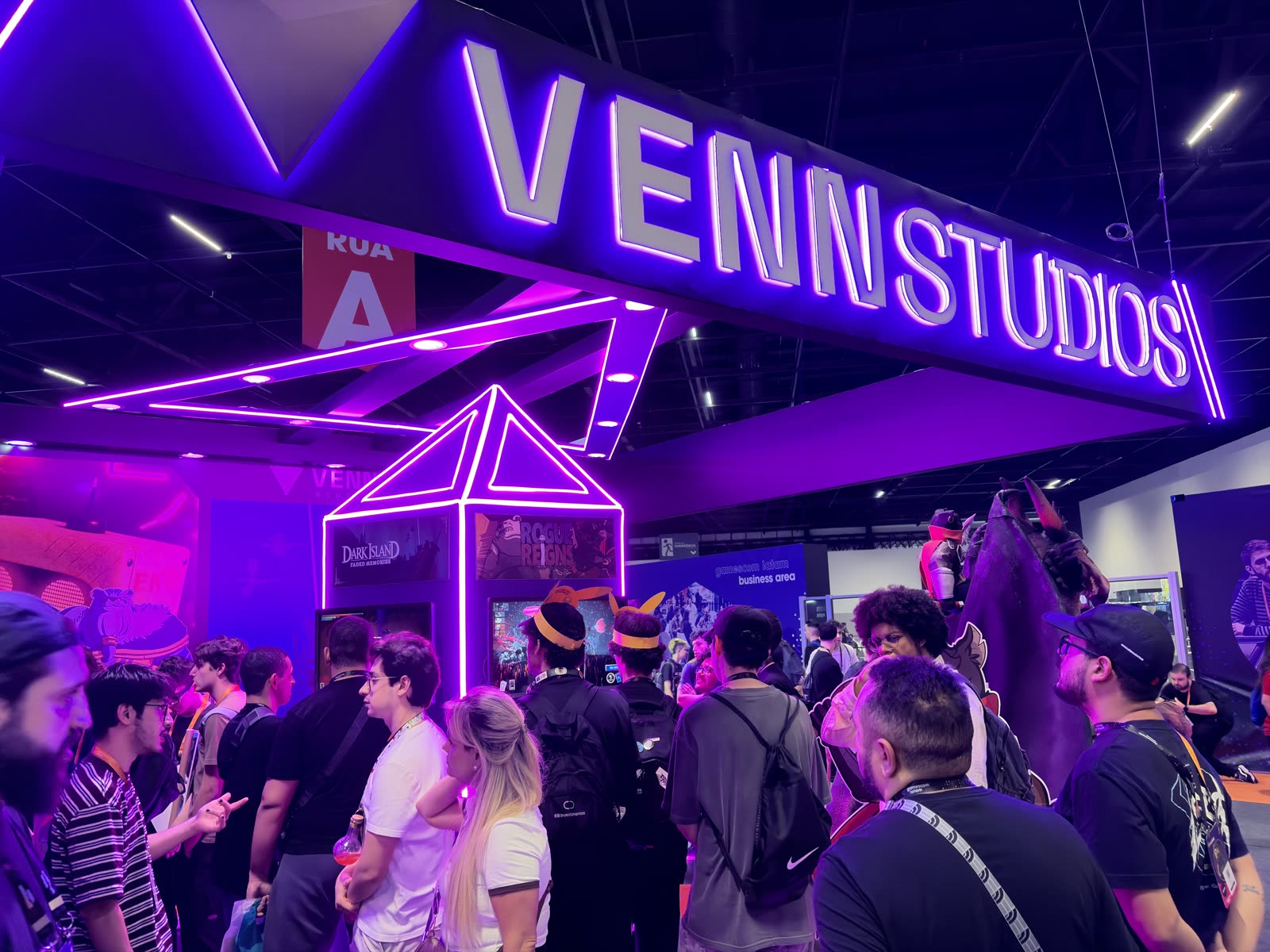A crowd gathered under the neon VENN STUDIOS sign at the booth